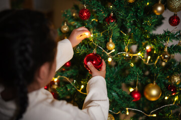 close up hand of childl decorating toy ball on Christmas tree in home at night