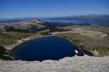 Fototapeta premium Mujer joven sentada en la cumbre del extinto volcán Batea Mahuida ubicado en la frontera entre Chile y Argentina. En el centro del volcán hay una laguna.