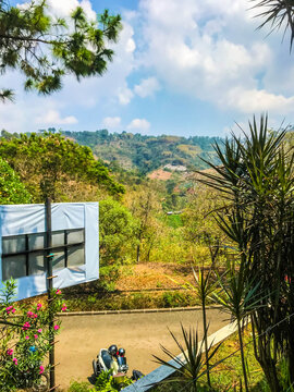Mountain landscape with lush green trees, blue sky, and clouds, viewed from a hillside road in Indonesia, showing natural scenery and peaceful outdoor atmosphere.