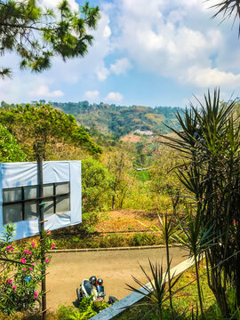 Mountain landscape with lush green trees, blue sky, and clouds, viewed from a hillside road in Indonesia, showing natural scenery and peaceful outdoor atmosphere.