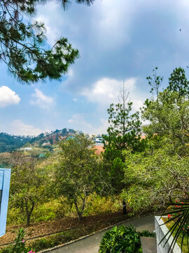 Mountain landscape with lush green trees, blue sky, and clouds, viewed from a hillside road in Indonesia, showing natural scenery and peaceful outdoor atmosphere.