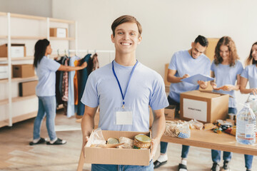 A group of volunteers works together at a community center, packing donations into boxes. One volunteer smiles while holding a box of goods, while others organize supplies and take notes.