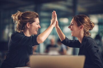 Celebrating success two women high-fiving at desk in modern office environment