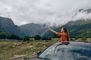 Fototapeta premium A woman leans from a sunroof of a car in a rural valley, pointing toward distant mountains, capturing a moment of adventure, freedom, and exploration in open countryside