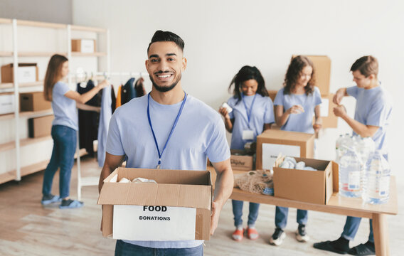 A group of volunteers is organizing food donations at a community center. One person smiles while holding a box labeled food donations, and others are focused on packing. - Powered by Adobe