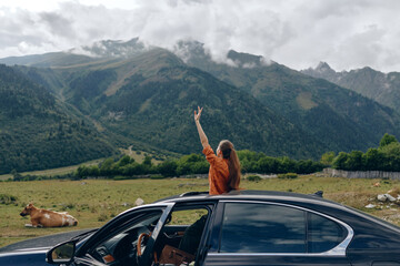 Fototapeta premium woman car mountains meadow cow roadtrip nature travel sunroof, woman standing through sunroof in meadow with cow and peaks, authentic inclusivity joyful freedom relaxed smile