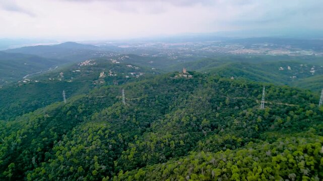 Epic Barcelona Torre Baro forest aerial reveal. 
Cinematic 4K drone forward push-in and 
orbit reveal of historic stone tower castle 
on green mountain hill in Spain.
