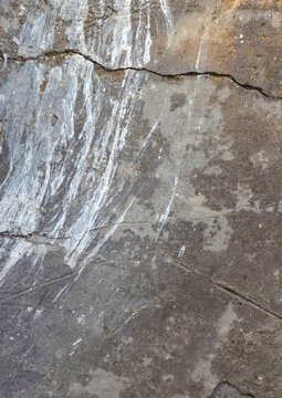 A close-up vertical shot of a rough grey concrete wall texture featuring deep cracks, white stains, and a grunge weathered surface for abstract backgrounds.