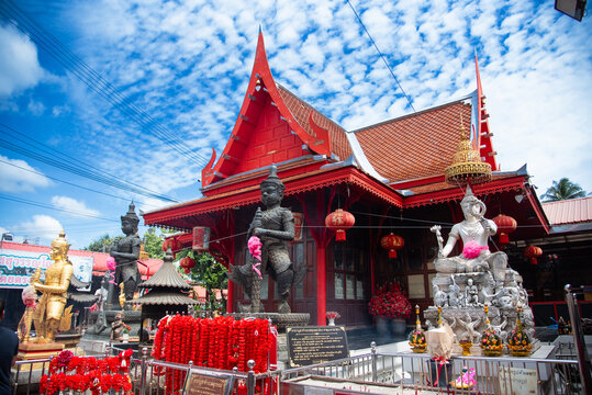 Red wooden pavilion at a Thai temple shrine dedicated to Thao Wessuwan. The area is decorated with red lanterns and garlands for worship.