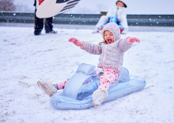 Joyful Children Sledding Down a Snowy Hill - Winter Fun and Laughter on Inflatable Sleds. Winter Thrill Ride
