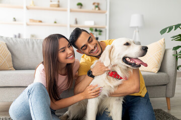 A young couple enjoys a playful moment with their golden retriever in a bright living room filled with plants and cozy decor. They share smiles and affection with their pet.