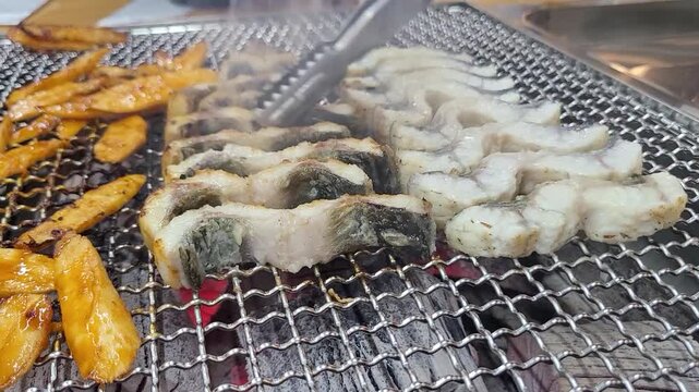 숯불과 철판 위에서 장어구이와 더덕구이를 함께 굽는 한국 음식 조리 장면