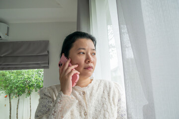 Asian Woman Talking Seriously on a Pink Smartphone Near a Bright Window