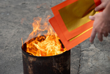 Burning gold and silver paper offering to ancestors. Close-up of fire consuming spirit money in a traditional Asian ceremony. Concept of belief and filial piety.