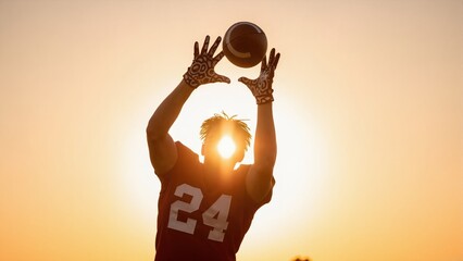 Silhouette of football player catching ball at sunset. American football receiver making catch against golden hour sun. Sports athlete in action