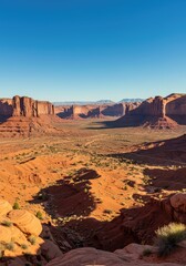 Fototapeta premium A massive, sun-drenched valley stretching out beneath towering red sandstone formations and cliffs under a bright blue sky ,blue ,cliff ,mesa