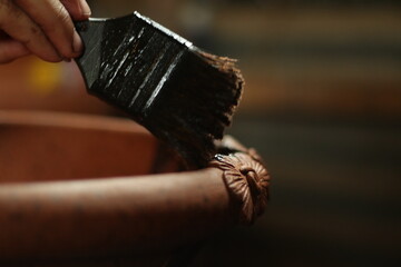 Close-up of an artisan hand painting a textured clay craft, highlighting traditional craftsmanship, natural materials, and detailed handmade artwork in warm earthy tones.