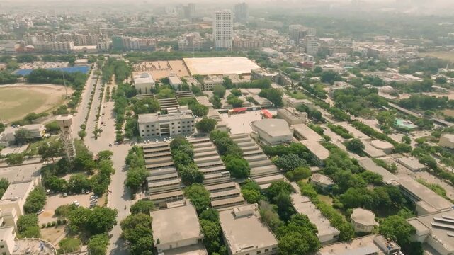 Forward aerial glide and pan over the modern NED University of Engineering and Technology campus in Karachi during an intense sunny hazy day, with sprawling city in the background.