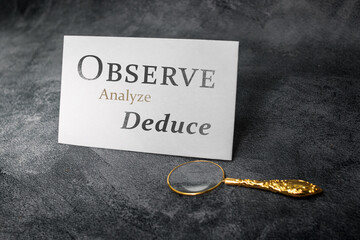 A motivational card displaying the words “Observe, Analyze, Deduce” stands on a textured...