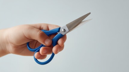 A child's hand holds blue kid-safe scissors. The focus is on the hand and the scissors. Clean background highlights the action. Captured with minimal distractions in light studio setting