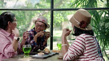 Asian senior female friends playfully teasing and pointing during friendly chat around cafe table while laughing and sipping drinks in joyful retirement moment filled with fun and connection