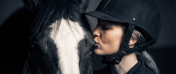 Woman kisses horse in stable during training session at dusk