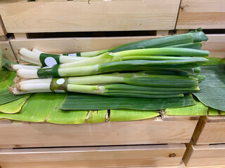 Bunches of fresh Japanese bunching onions or Negi wrapped in banana leaf displayed on a wooden crate in a supermarket.