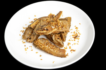 Crispy deep fried small fish topped with golden garlic served on white round plate.