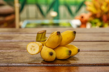 A bunch of small yellow ripe bananas with one cut open showing the inside on a wooden table.