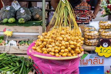 A pile of fresh yellow Barhi dates displayed in a basket with pink net at a fruit market stall.