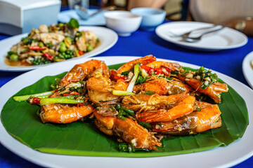 Delicious stir fried prawns with salt and chili served on green banana leaf on white plate.