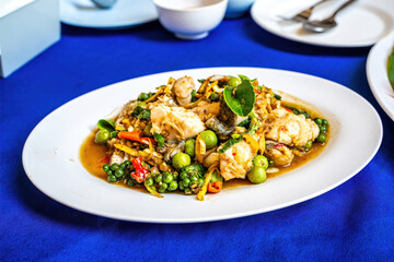 Authentic Thai spicy stir fried fish with green peppercorns and herbs on white plate.
