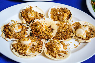 Grilled scallops in shells topped with crispy garlic and butter served on white plate.