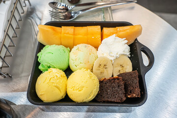 Dessert plate with fresh orange melon slices, colorful ice cream scoops and brownie.