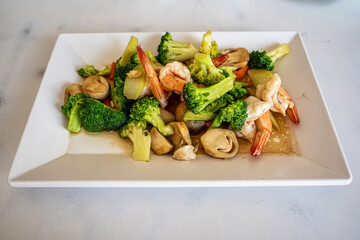 Healthy stir fried broccoli with fresh shrimp and mushrooms served on white square plate.