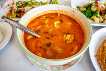 Traditional Thai spicy tom yum seafood soup with shrimp and mushrooms in white bowl.