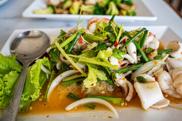 Authentic Thai spicy glass noodle salad with squid and shrimp served on white rectangular plate.