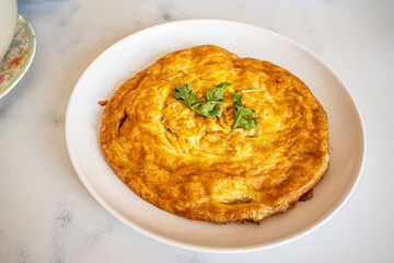 Golden brown Thai style fluffy omelet with coriander topping served on white plate.