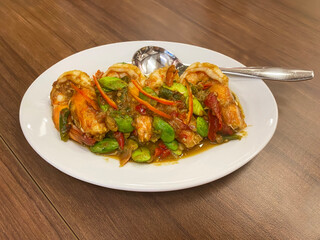 Spicy stir fried shrimp with stink bean and shrimp paste served on white plate on wooden table.