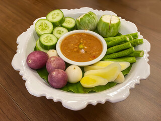Spicy shrimp paste chili dip served with fresh mixed vegetables on elegant white pedestal plate.