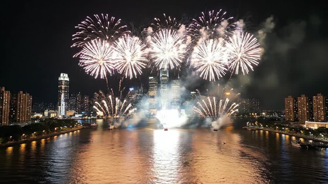 Drone aerial night view of big city skyline above river, massive colorful fireworks exploding, reflections on water, smooth forward flight, celebration stock style, ultra-realistic 4K