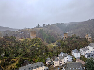 Obraz premium Esch-Sur-Sure, Wiltz, Grand Duche De Luxembourg, December 7, 2025, Castle Ruins Perched Atop Rugged Cliff Overlooking River And Village, Weathered Towers And Mossy