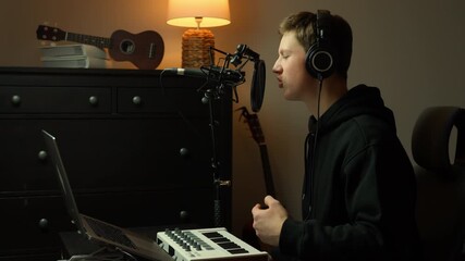 Young man recording vocals in a cozy home studio with headphones, professional microphone and laptop with MIDI keyboard, focused on producing and composing music in warm light - Powered by Adobe