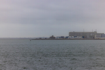 Den Helder, The Netherlands, Oktober 28th, 2024, A tranquil and serene view showcasing an industrial facility situated beside calm waters beneath a cloudy sky