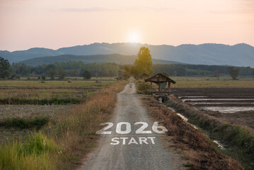 Fototapeta premium New Year 2026. Scenic rural landscape featuring a dirt path marked with 2026 start, surrounded by fields, trees, and mountains at sunrise, ideal for vision and future themes.