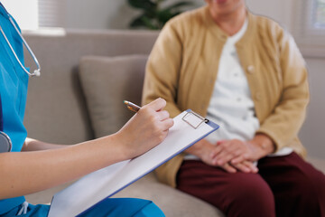 Nurse providing home care, writing on a clipboard during a health check up with an elderly patient...