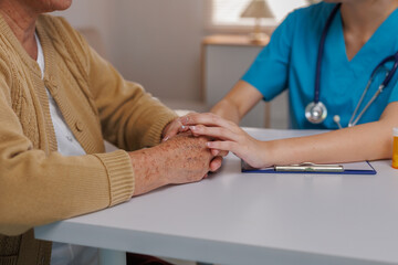 Nurse providing comfort and support, gently holding the hand of an elderly patient during a medical consultation at home