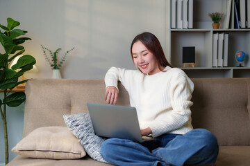 Young Asian woman smiling, enjoying remote work and online connection from home on a comfortable sofa, fostering work life balance