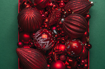 Merry Christmas and Happy New Year greeting card. Red Christmas ornaments with glitter in box on green background. Xmas and Winter holidays. Close up, top view