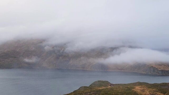 Severe foggy day on Unalaska, steep mountains fading into dense, low clouds. The heavy gray atmosphere create a dramatic, isolated environment typical of the remote Aleutian Islands, Alaska. 
